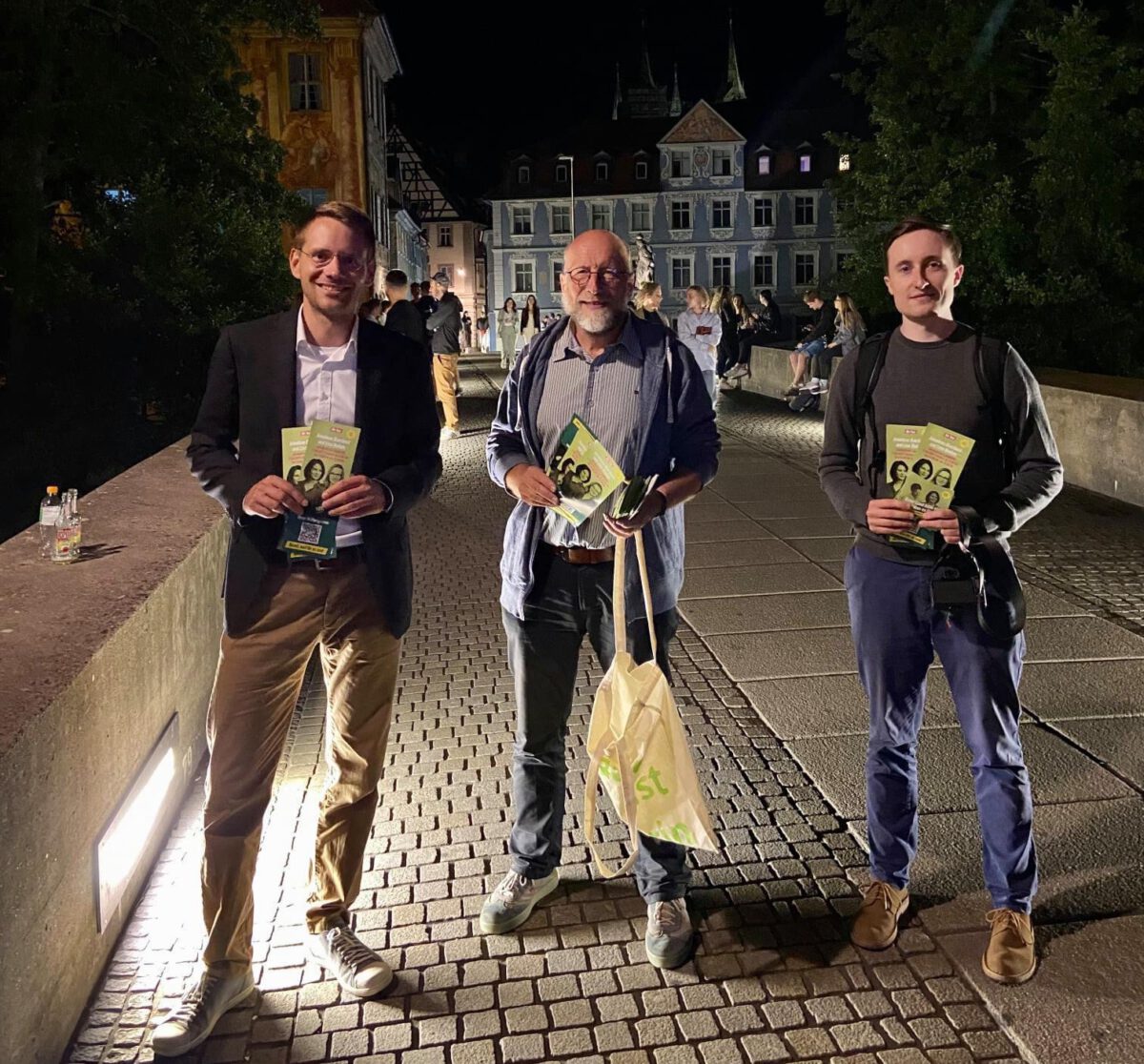 Thomas von Sarnowski mit zwei grünen Mitgliedern auf einer Brücke bei Nacht mit Flyern in der Hand