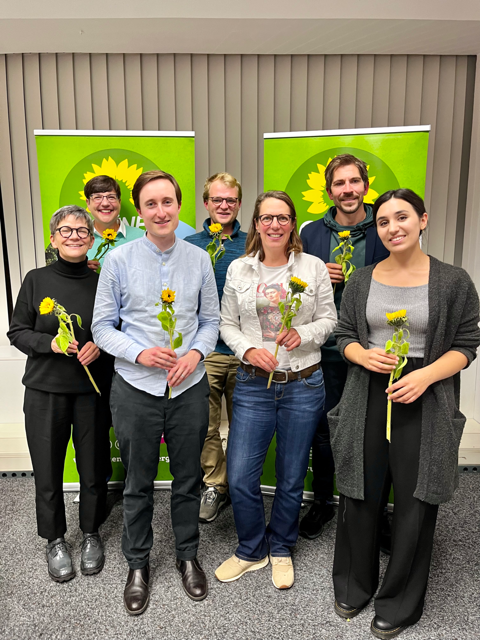 Die Mitglieder des neuen Stadtvorstands von Grünes Bamberg stehen vor zwei grünen Aufstellern mit Sonnenblume. In ihren Händen halten sie Sonnenblumen.