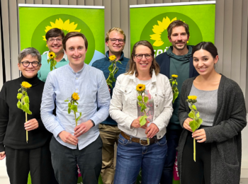 Die Mitglieder des neuen Stadtvorstands von Grünes Bamberg stehen vor zwei grünen Aufstellern mit Sonnenblume. In ihren Händen halten sie Sonnenblumen.