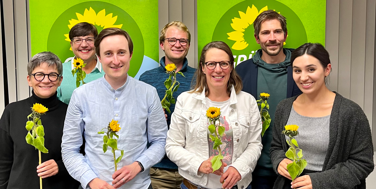 Die Mitglieder des neuen Stadtvorstands von Grünes Bamberg stehen vor zwei grünen Aufstellern mit Sonnenblume. In ihren Händen halten sie Sonnenblumen.